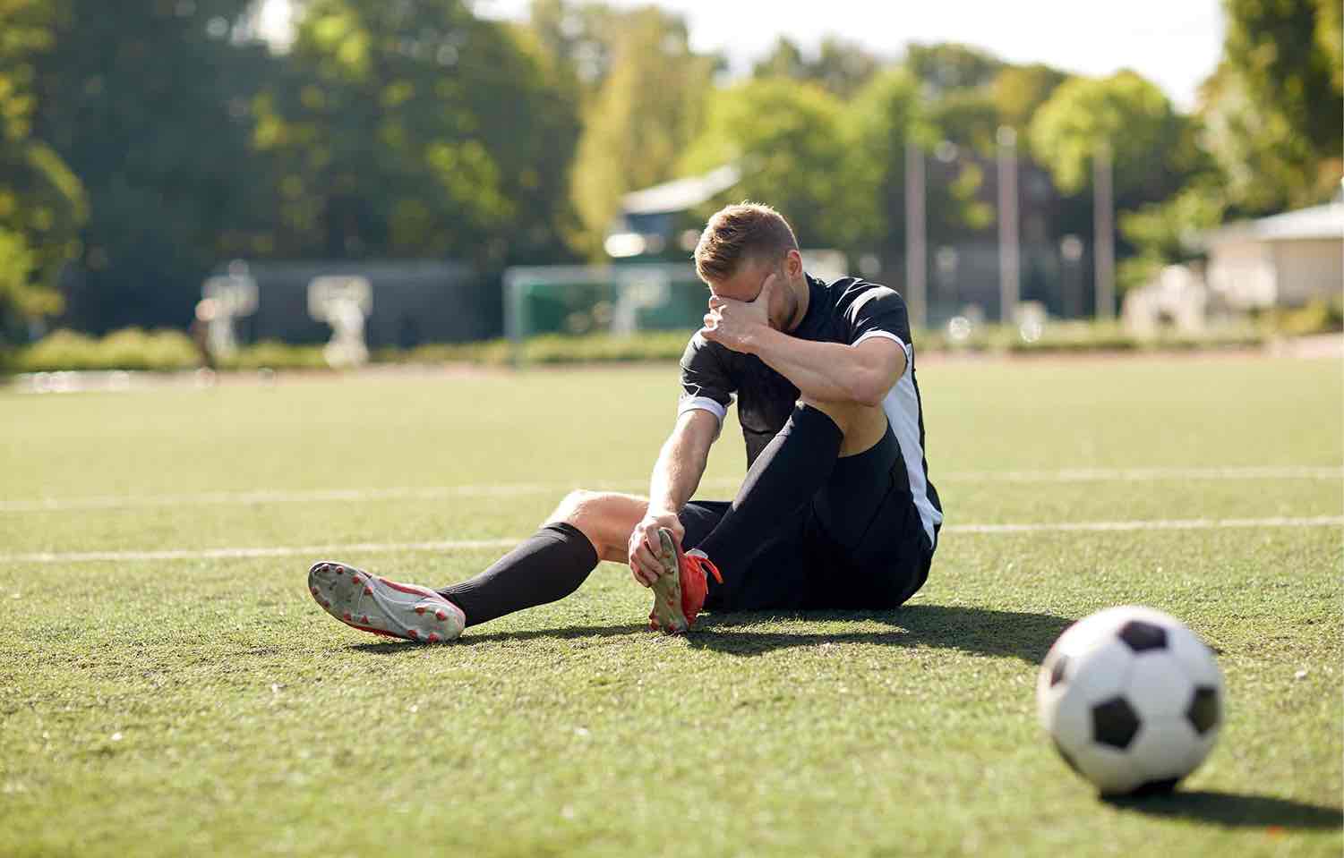 Football player on the pitch holding his knee after an injury, close-up of the knee